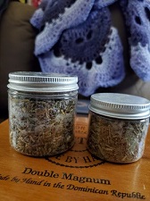 Two small mason jars filled with herbs atop a wooden table, with a purple and lavender crochet blanket in the background