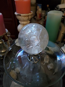 a crystal ball on a glass base with three candles in the background  